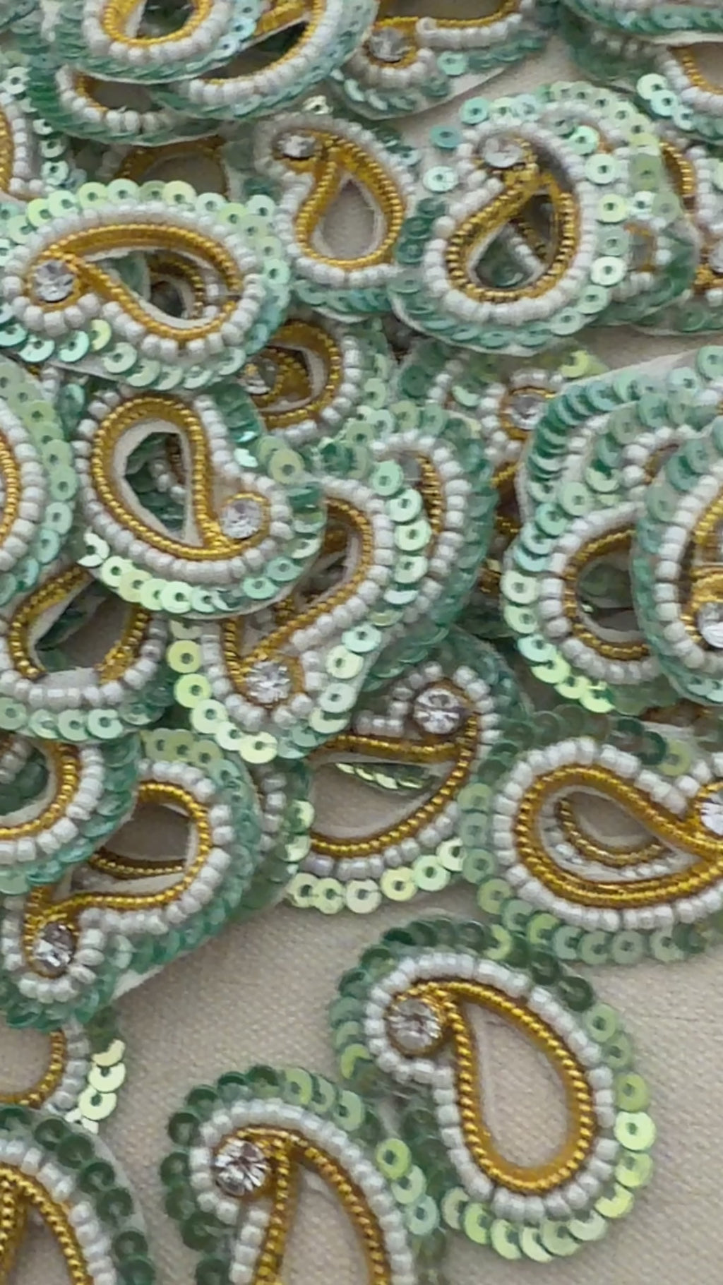 Collection of green and gold beaded paisley designs on a beige background
