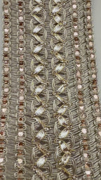 Decorative fabric trim with gold embroidery and a ruler for scale on a neutral background