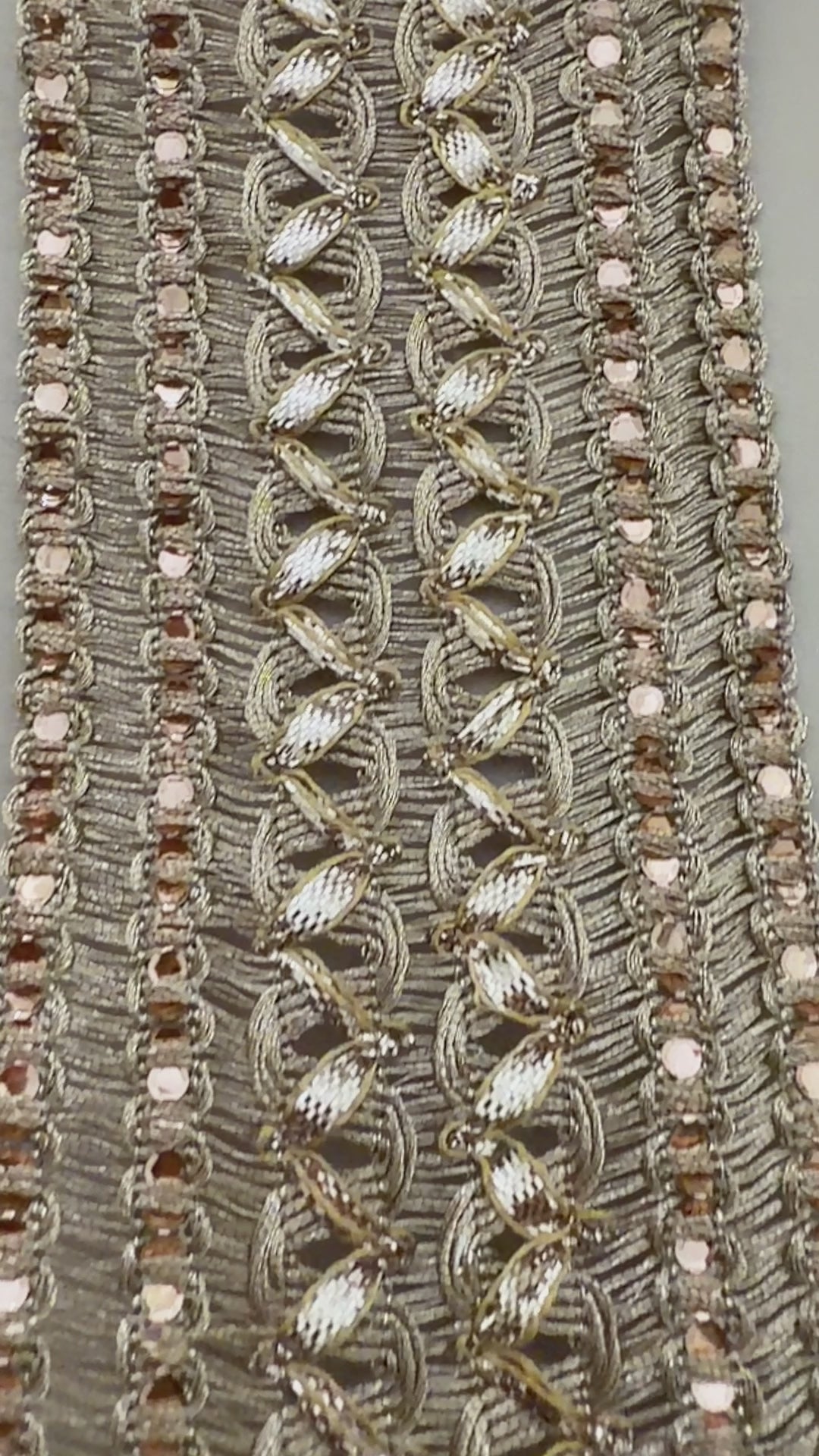 Decorative fabric trim with gold embroidery and a ruler for scale on a neutral background