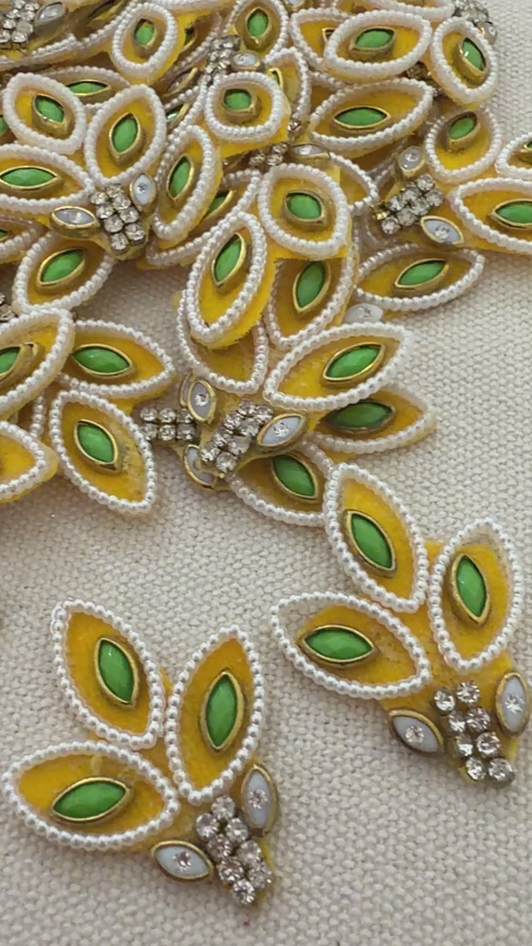 Decorative leaf-shaped embellishments with green and gold colors on a beige background.
