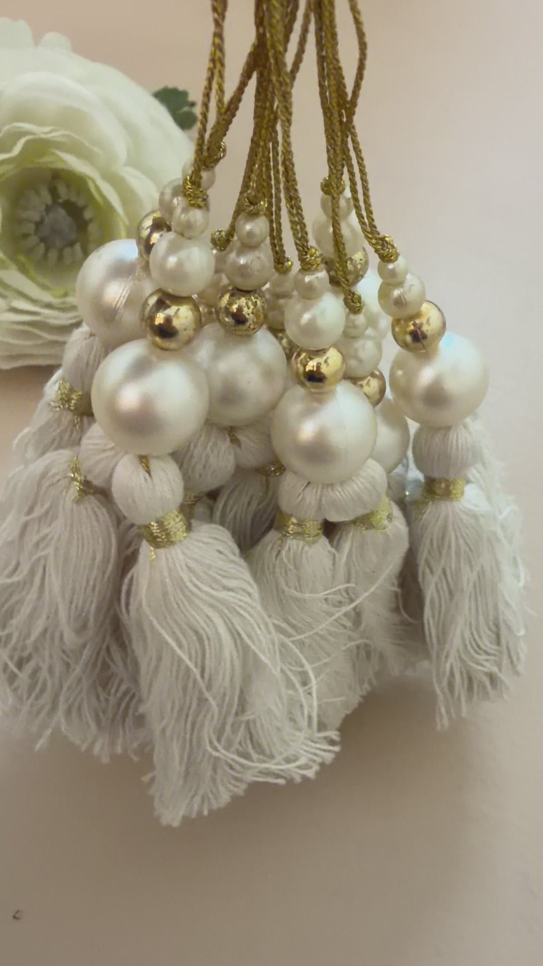 Necklace with white tassels and pearls on a beige background with a white flower.