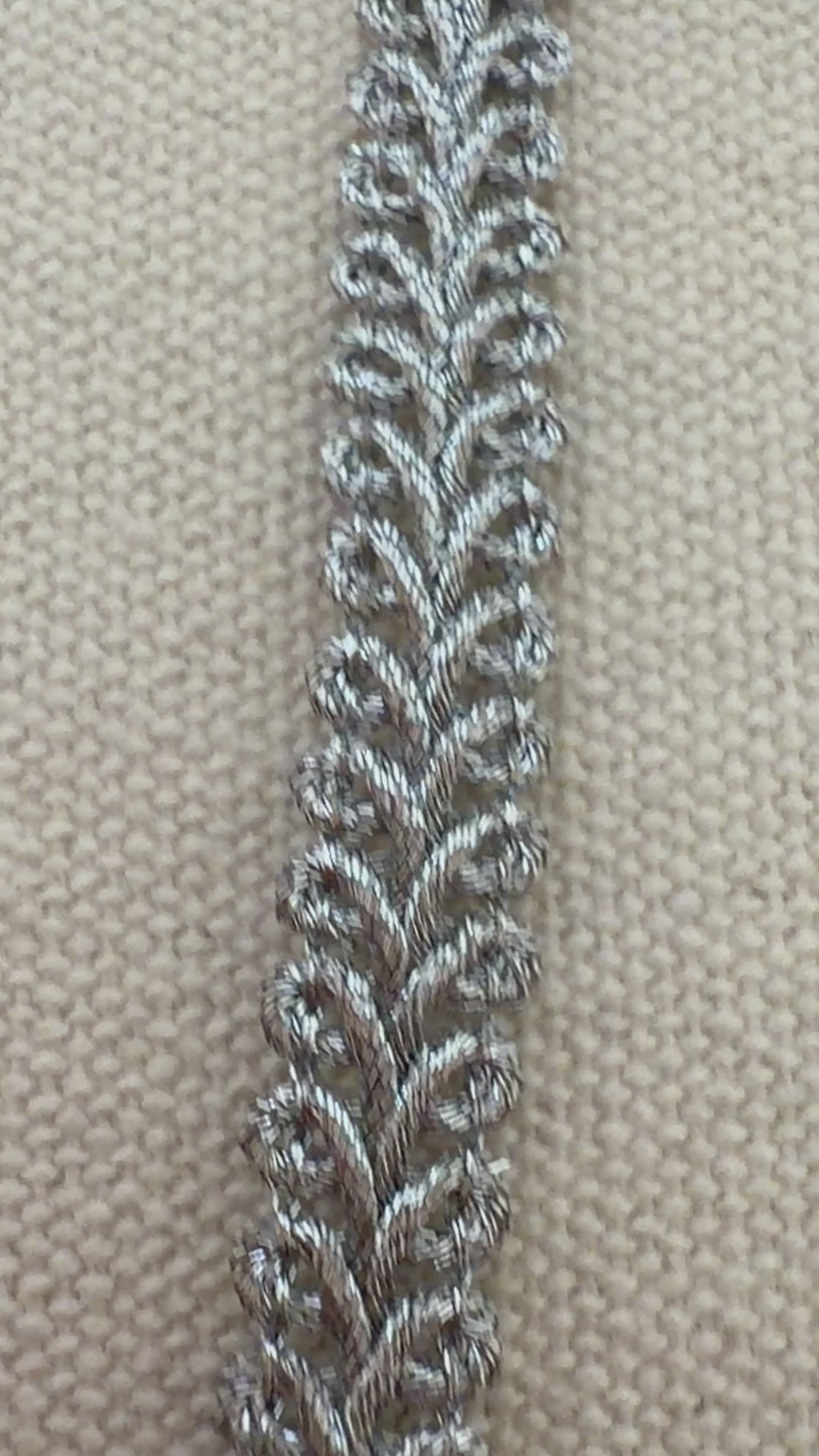 Spool of silver lace fabric on a beige background