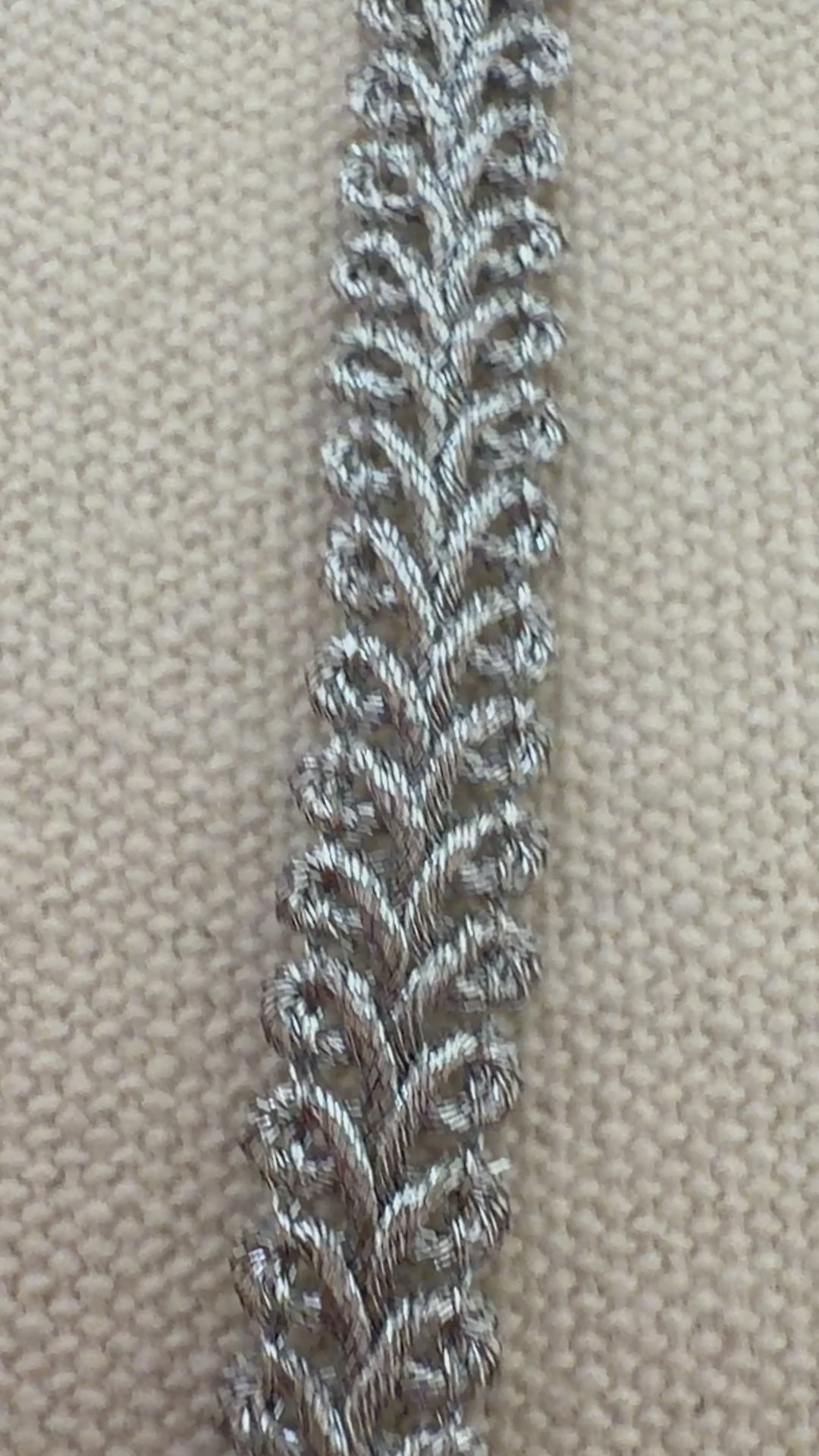 Spool of silver lace fabric on a beige background