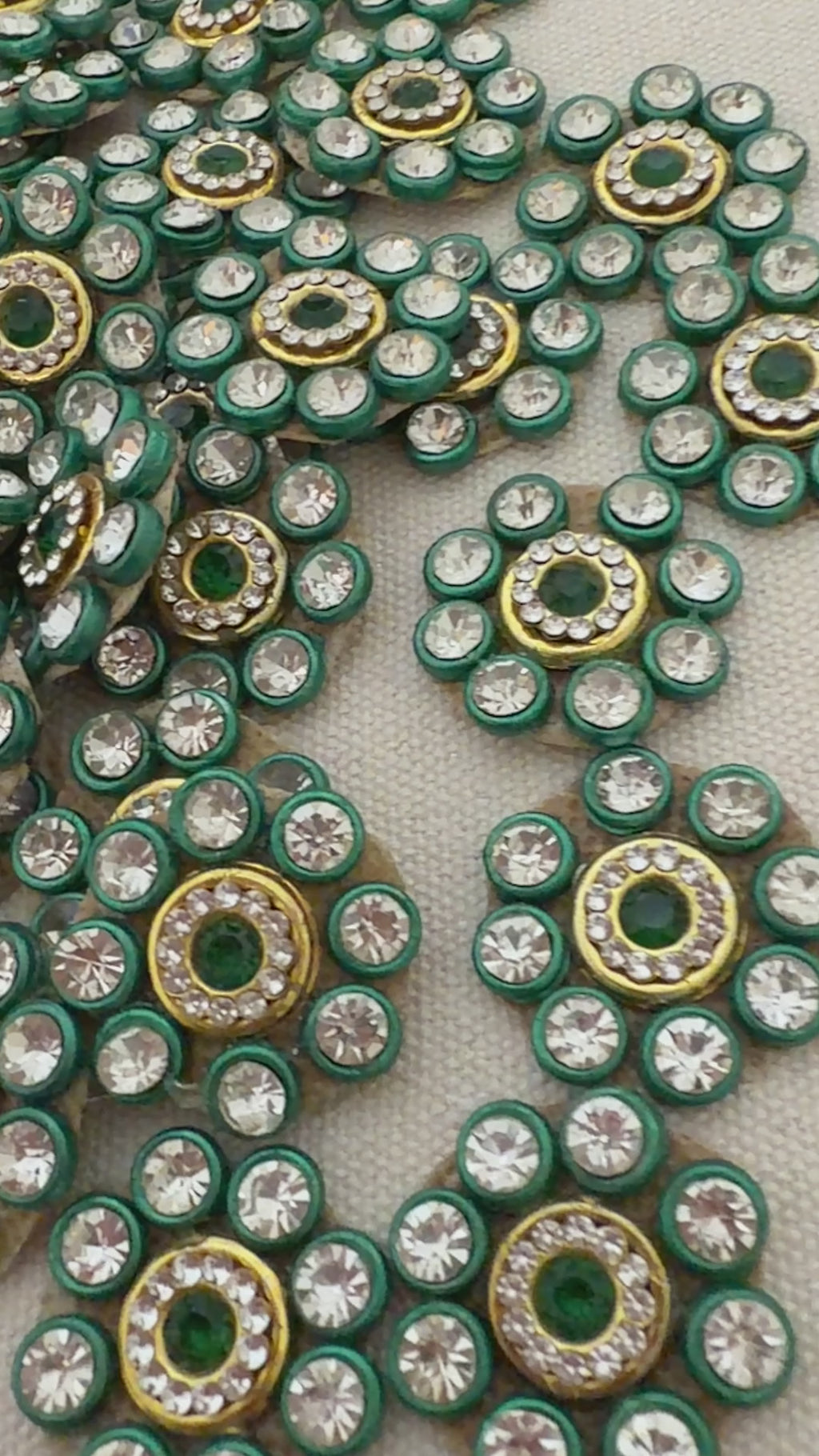 Close-up of decorative embellishments with green, gold, and clear stones on a gray background