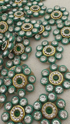 Close-up of decorative embellishments with green, gold, and clear stones on a gray background