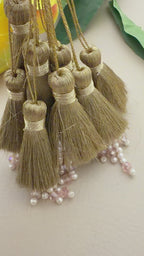 Gold tassels with pearl embellishments on a neutral background with yellow flowers.