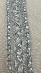 Silver decorative ribbon with intricate patterns on a beige background with a white flower.