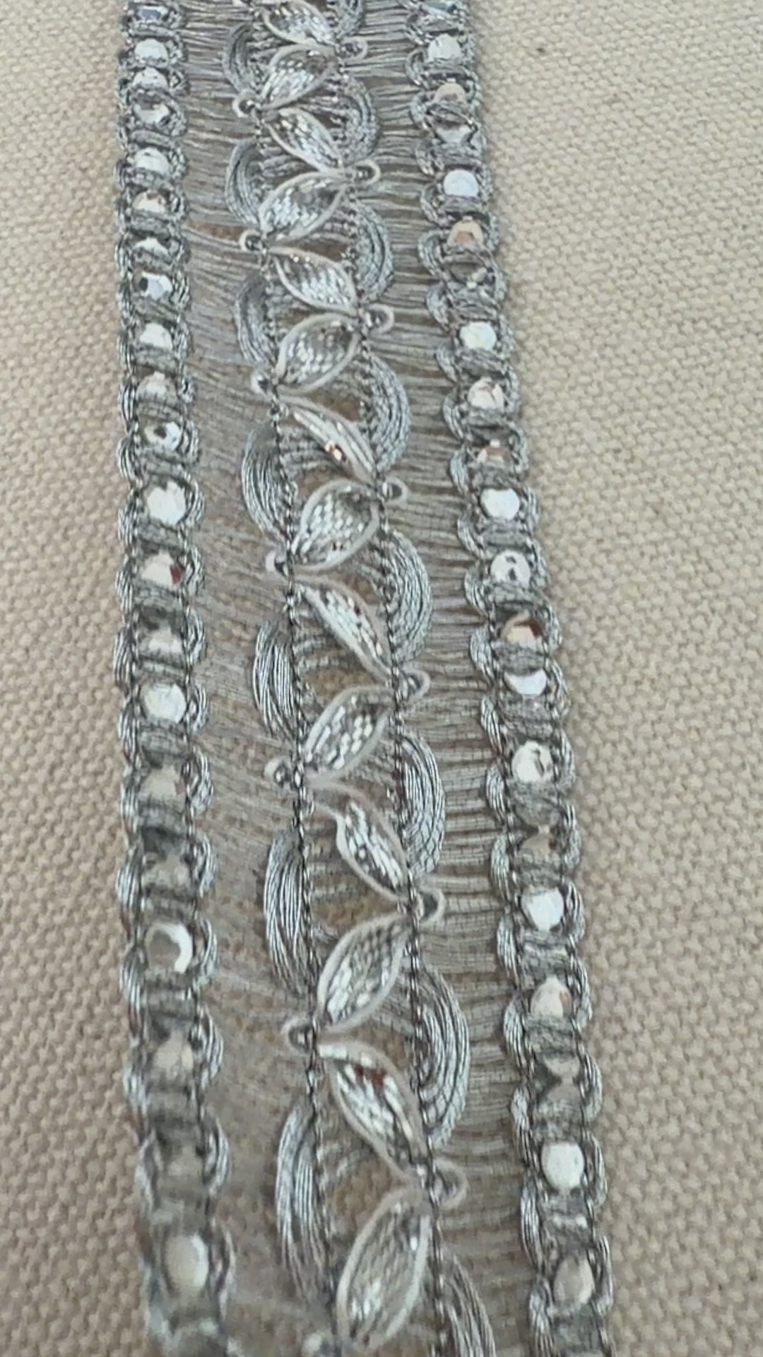 Silver decorative ribbon with intricate patterns on a beige background with a white flower.