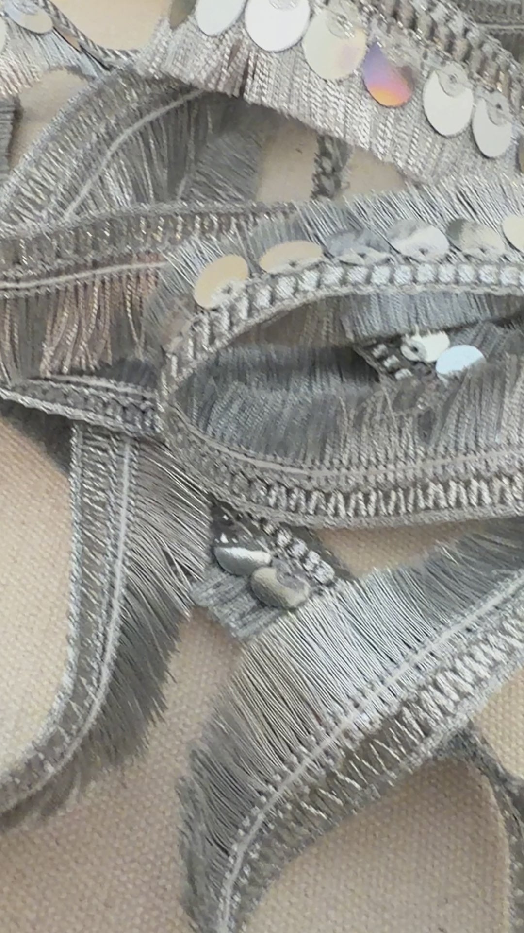 Roll of silver sequin ribbon on a beige fabric background with a white flower.