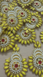 Decorative yellow and gold brooch with red gemstone next to a ruler for scale on a beige background