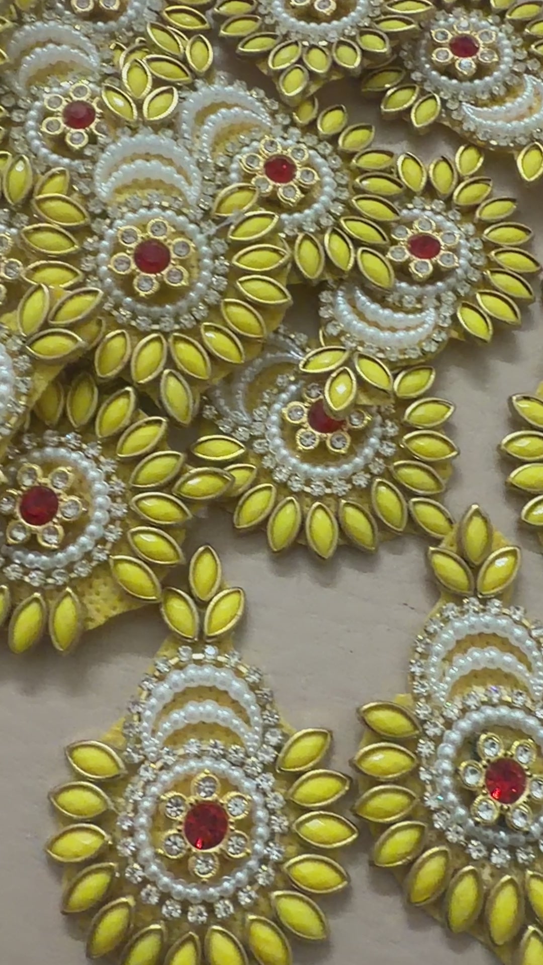 Decorative yellow and gold brooch with red gemstone next to a ruler for scale on a beige background