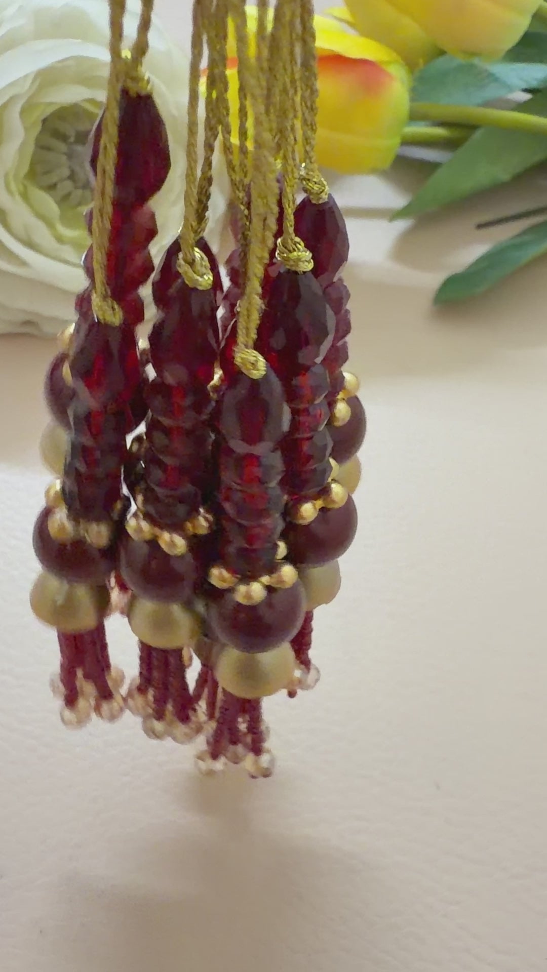 Decorative hanging with red beads and gold accents on a light gray background