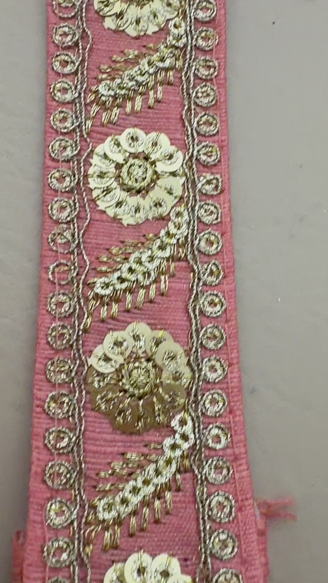 Decorative pink ribbon with gold floral embroidery held between fingers