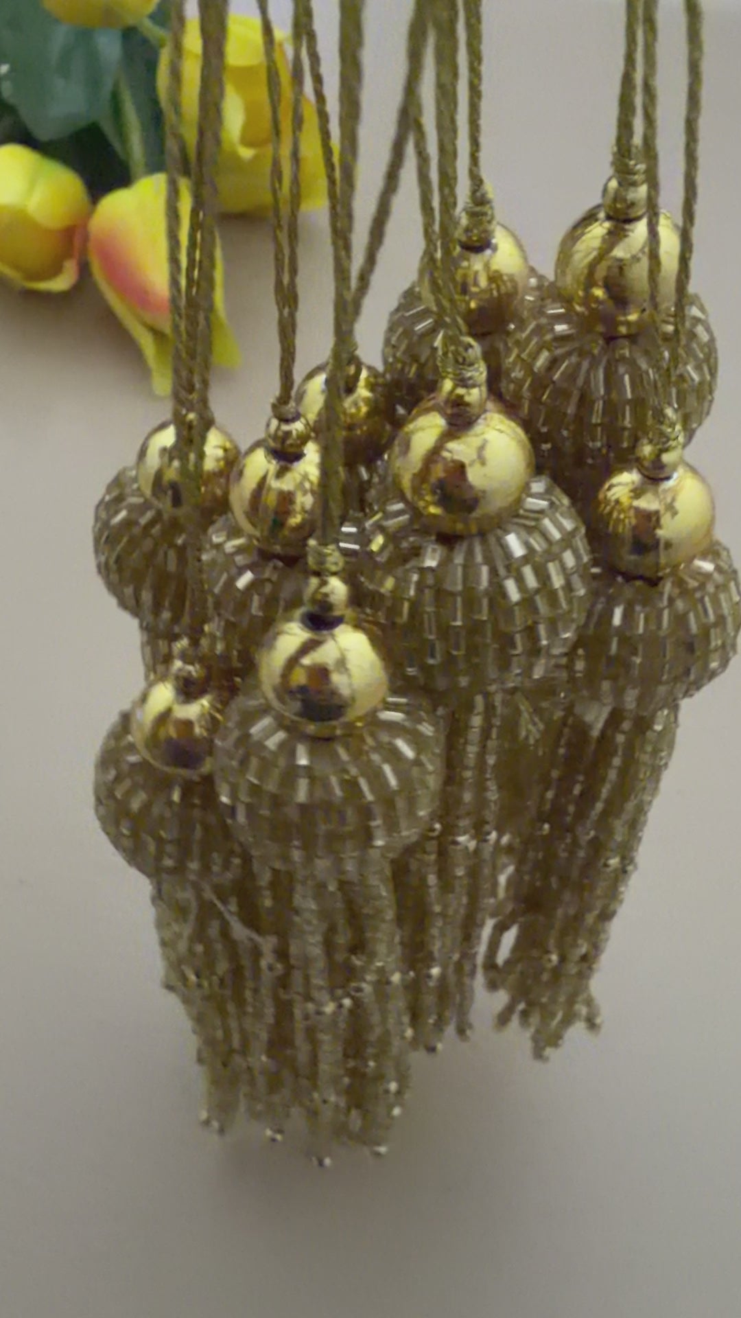 Gold tassel with decorative beads next to a ruler on a light gray background