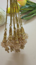 Decorative gold pendant with beads and crystals next to a ruler on a light gray background