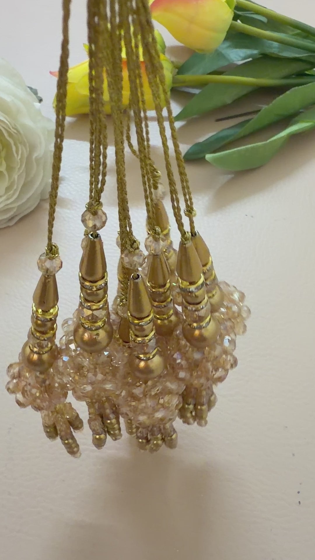 Decorative gold pendant with beads and crystals next to a ruler on a light gray background