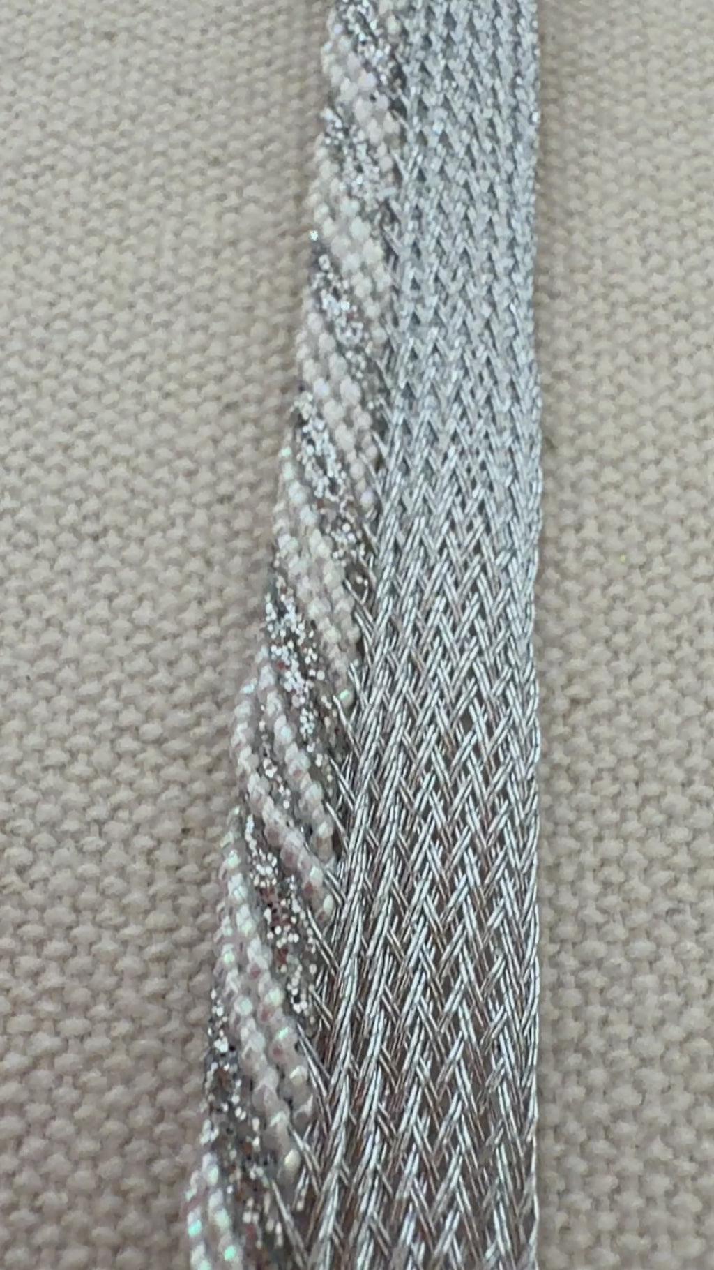 Hand holding a strip of silver metallic ribbon with a blurred floral background