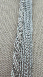 Hand holding a strip of silver metallic ribbon with a blurred floral background
