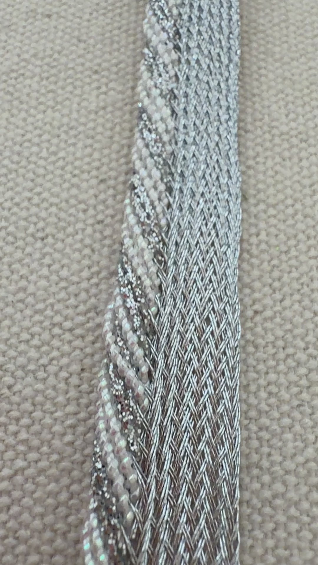 Hand holding a strip of silver metallic ribbon with a blurred floral background