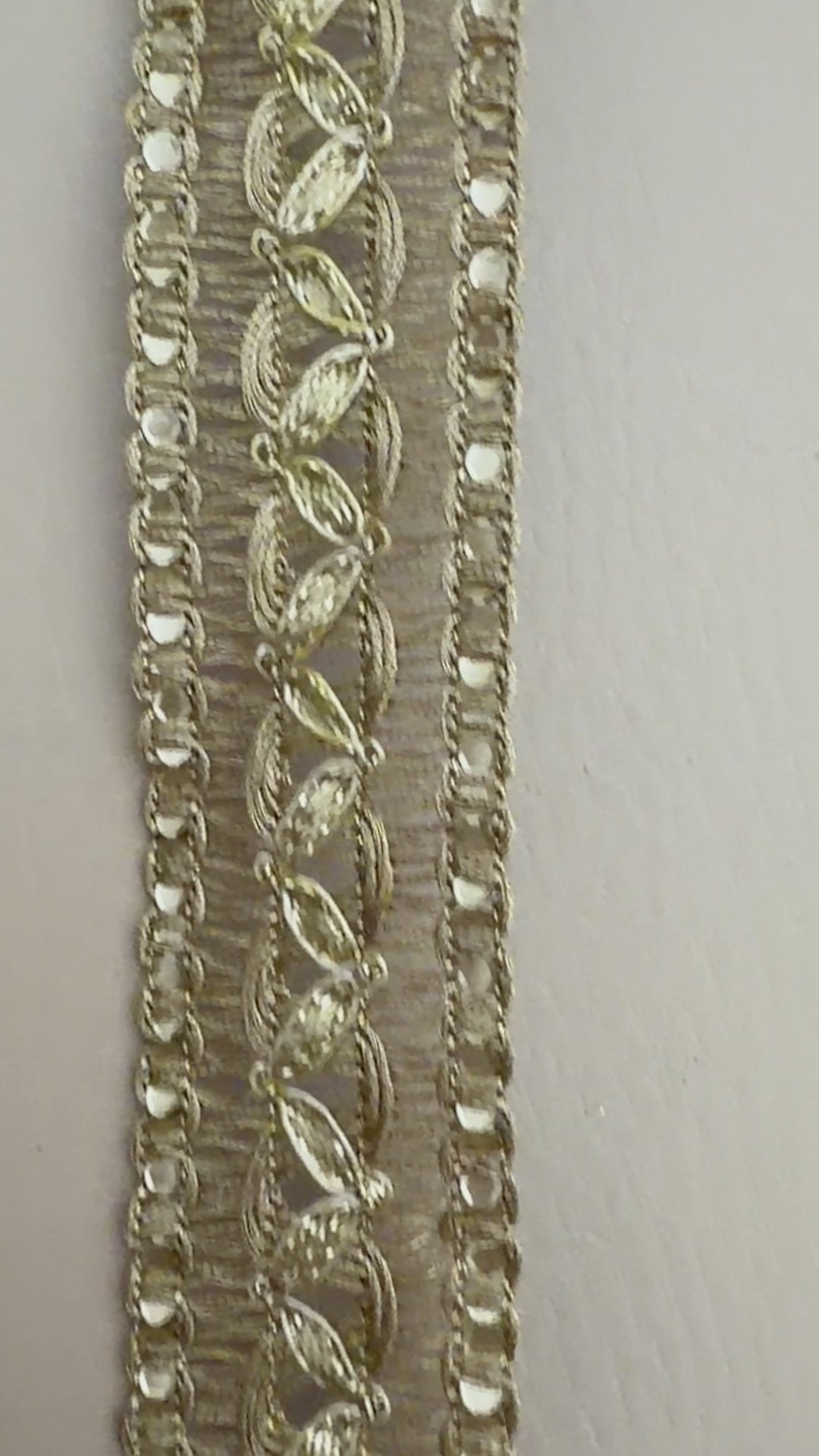 Decorative gold lace fabric with a ruler for scale on a neutral background
