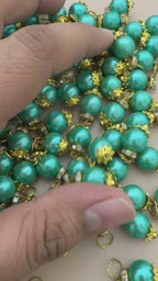 Turquoise pearl-like beads with gold accents on a light gray background