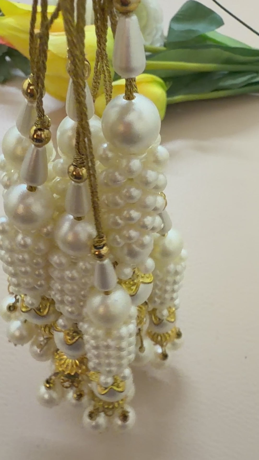 Pearl and gold decorative item next to a ruler on a beige background