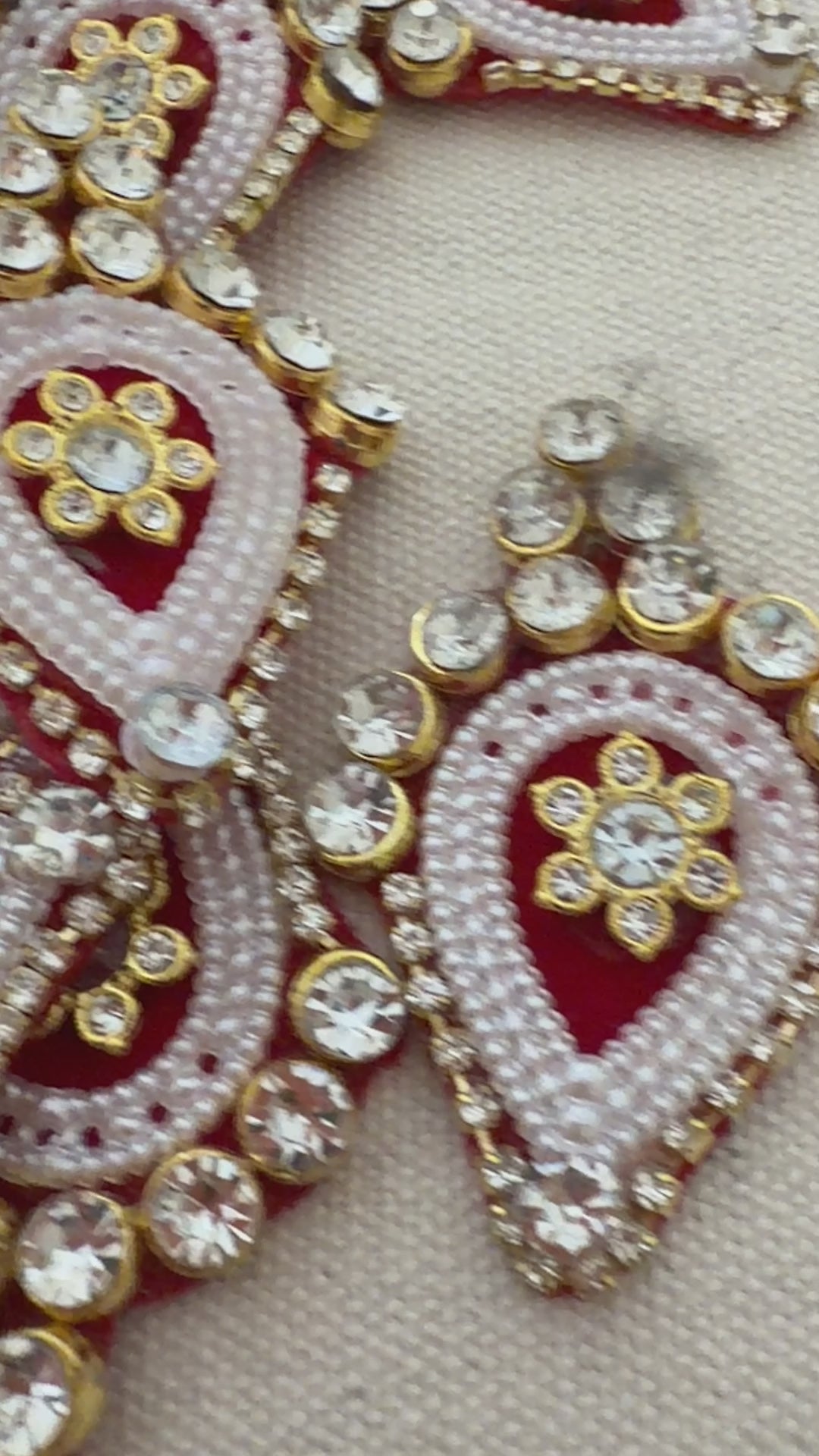 Ornate earrings with red, white, and gold colors on a textured beige background