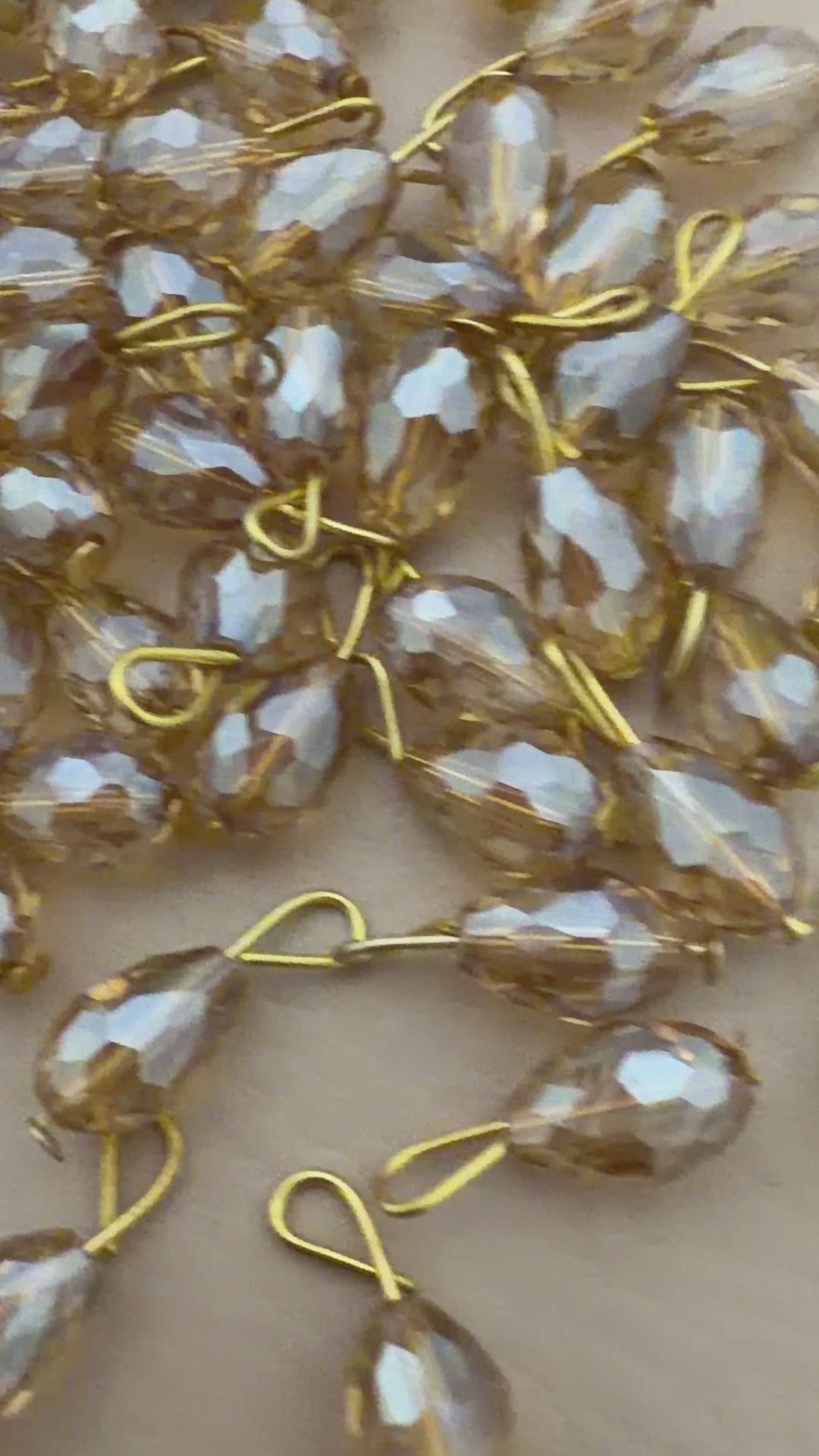 Gold and silver teardrop-shaped jewelry components on a beige background