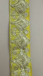 Roll of yellow lace ribbon with floral patterns next to a white flower on a light background