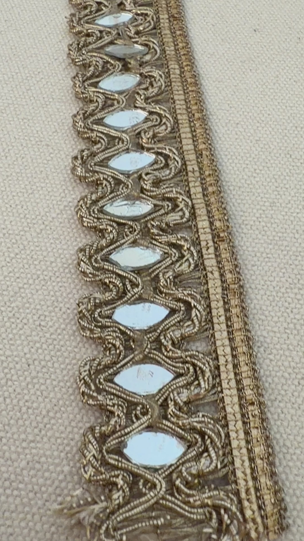 Decorative lace trim with reflective stones on a beige fabric background