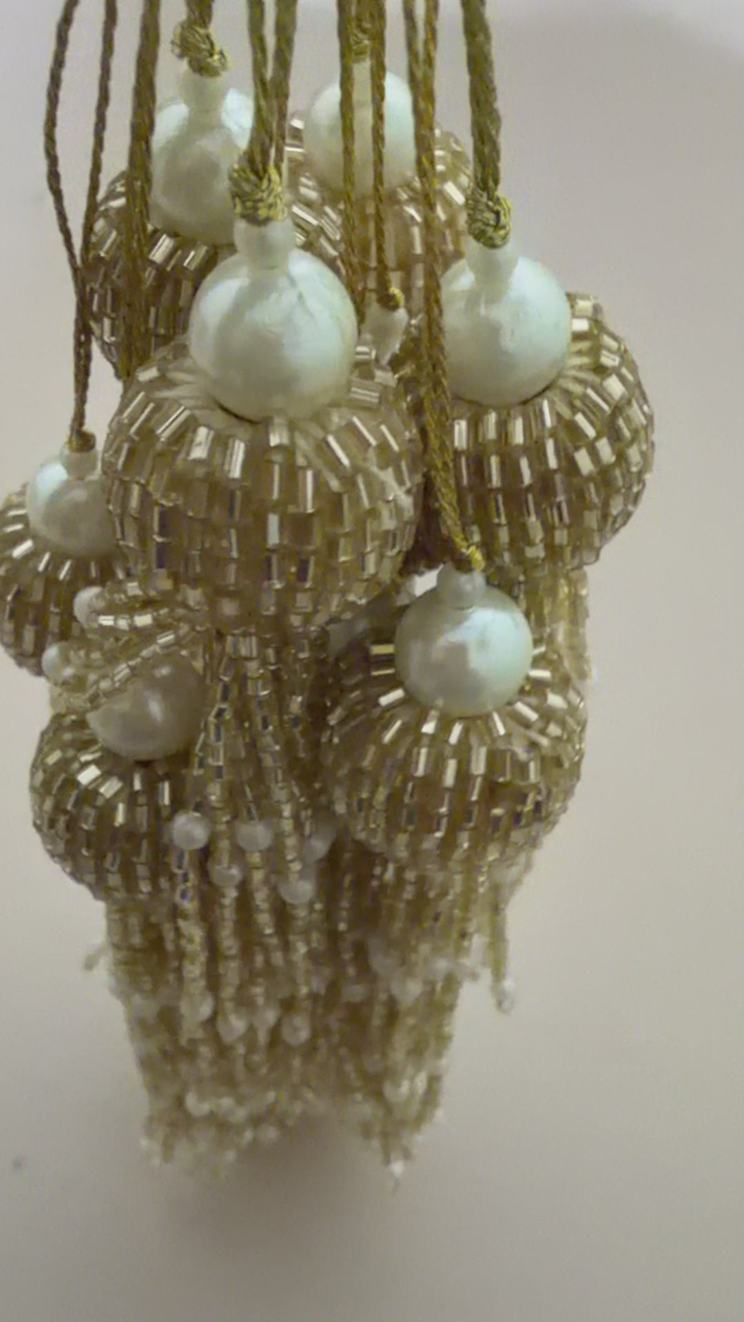 Gold tassel earrings with pearls next to a wooden ruler on a beige background