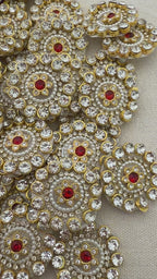 Close-up of decorative circular embellishments with gold, red, and clear stones on a beige background