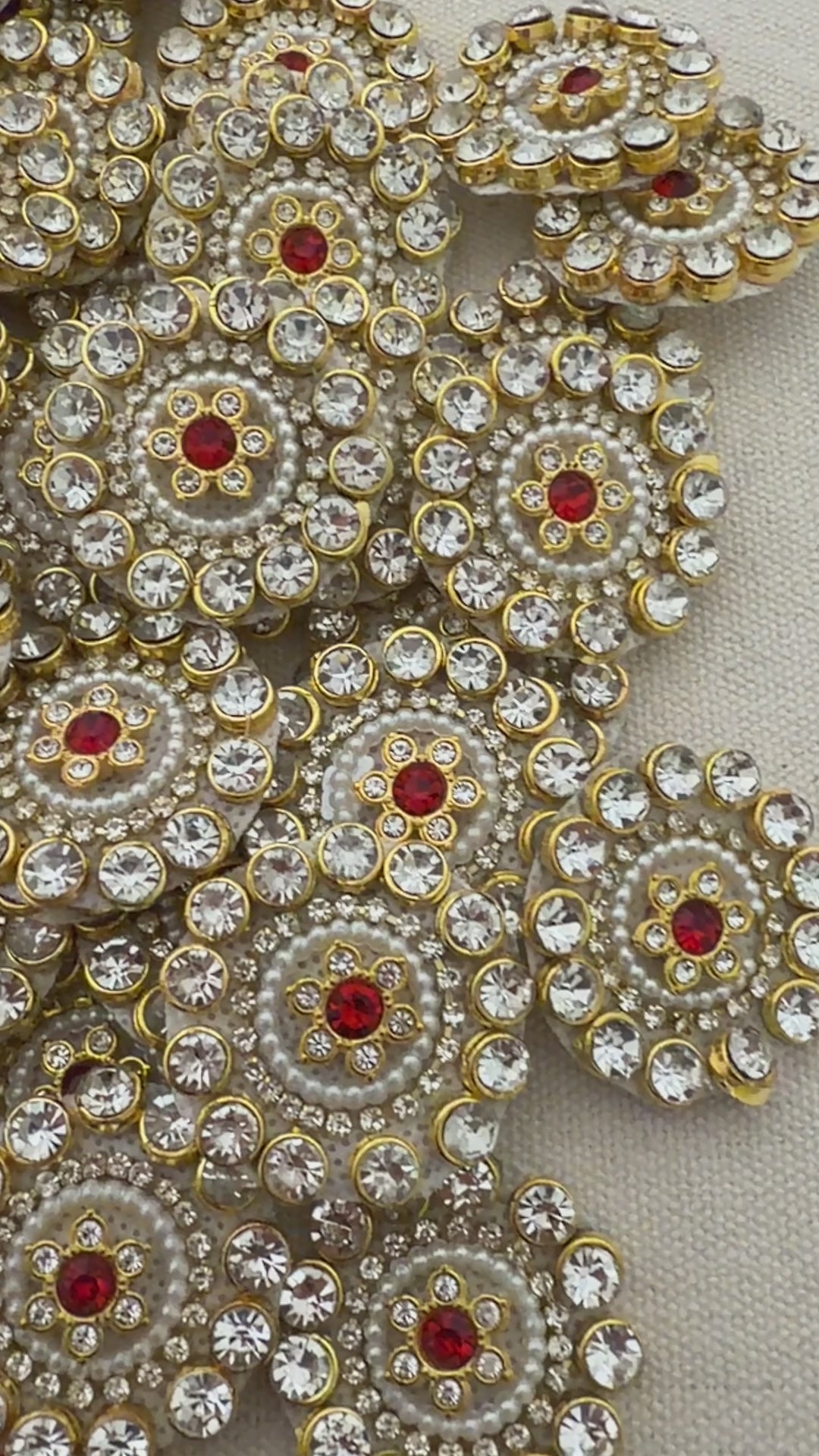 Close-up of decorative circular embellishments with gold, red, and clear stones on a beige background