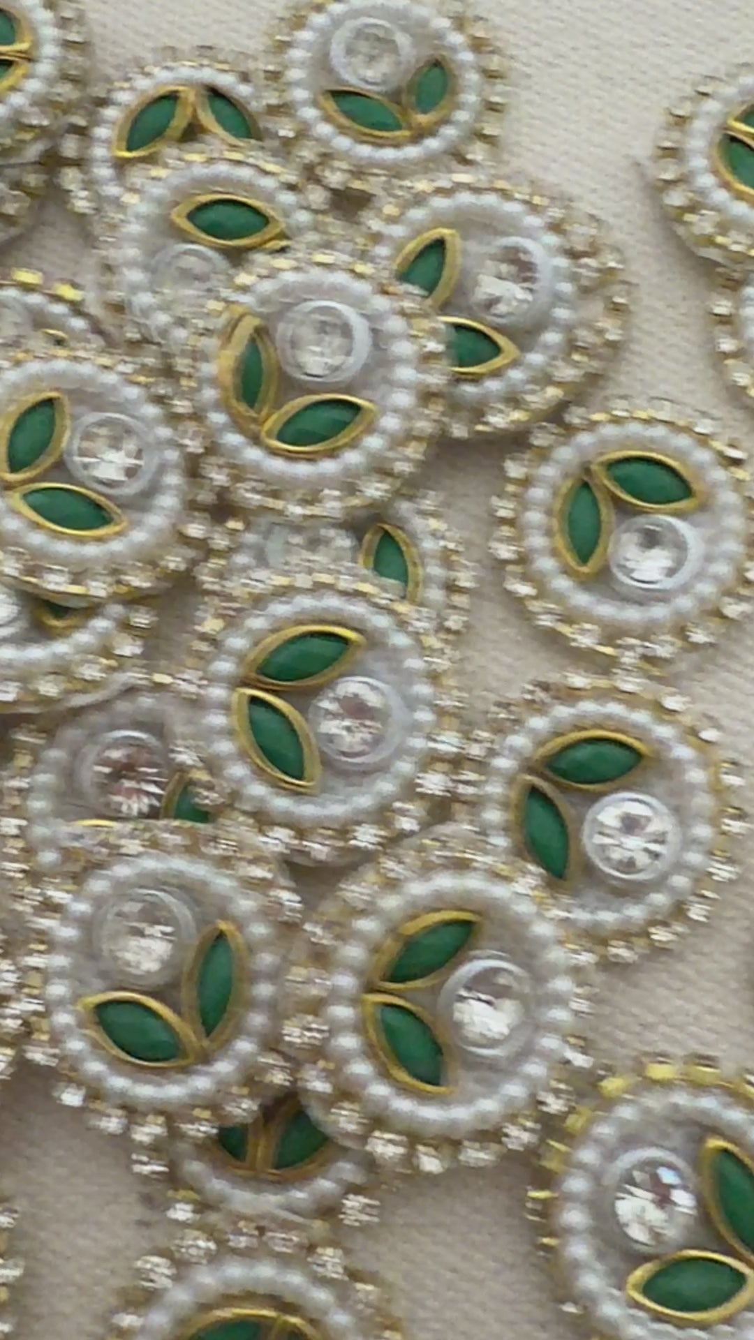 Close-up of decorative elements with pearls, green leaves, and crystals on a beige background