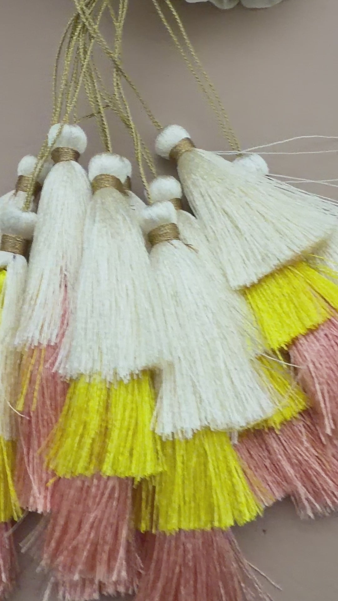 Set of tassels with white, yellow, and pink fringes on a light gray background