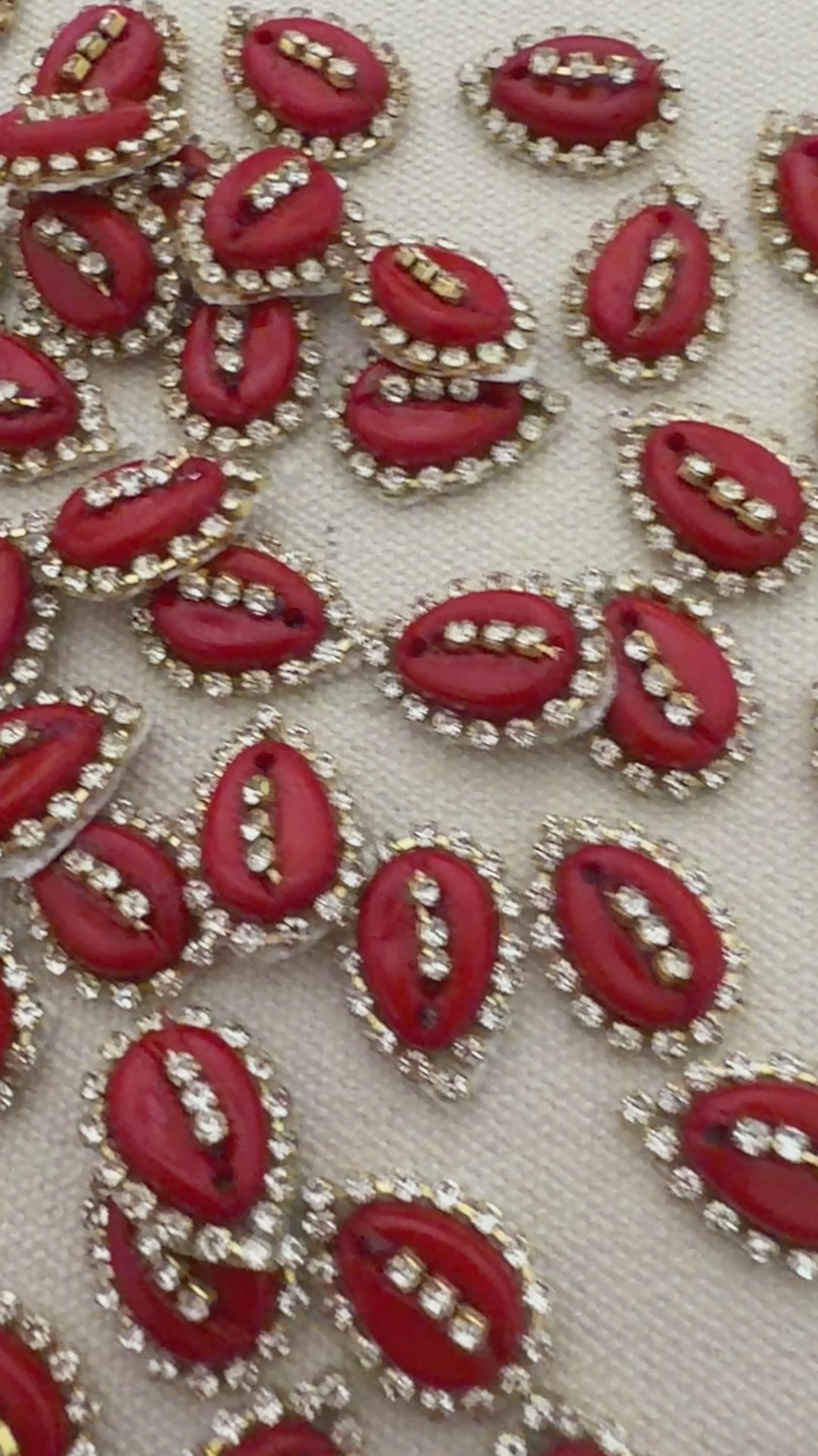 Red oval stones with gold and clear gemstone accents on a textured beige background