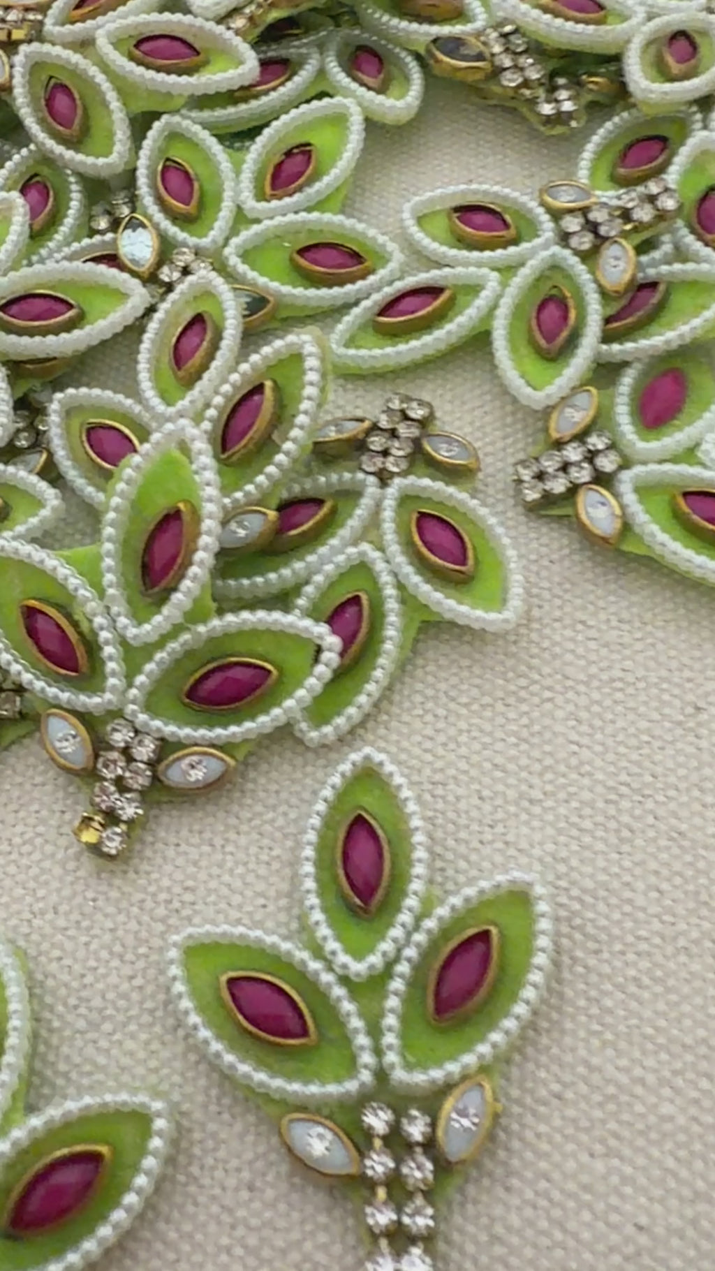 Decorative green and pink brooch held between fingers with a detailed embroidered background.