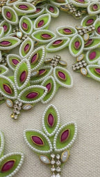 Decorative green and pink brooch held between fingers with a detailed embroidered background.