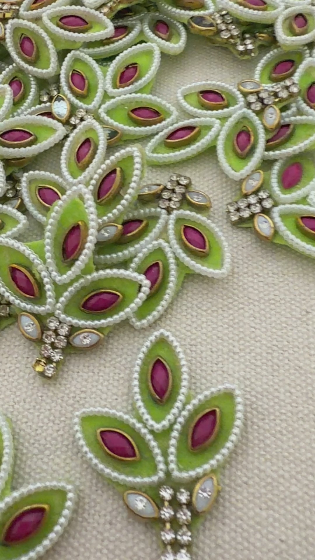 Decorative green and pink brooch held between fingers with a detailed embroidered background.