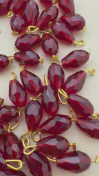 Red teardrop-shaped beads with gold loops on a light beige surface