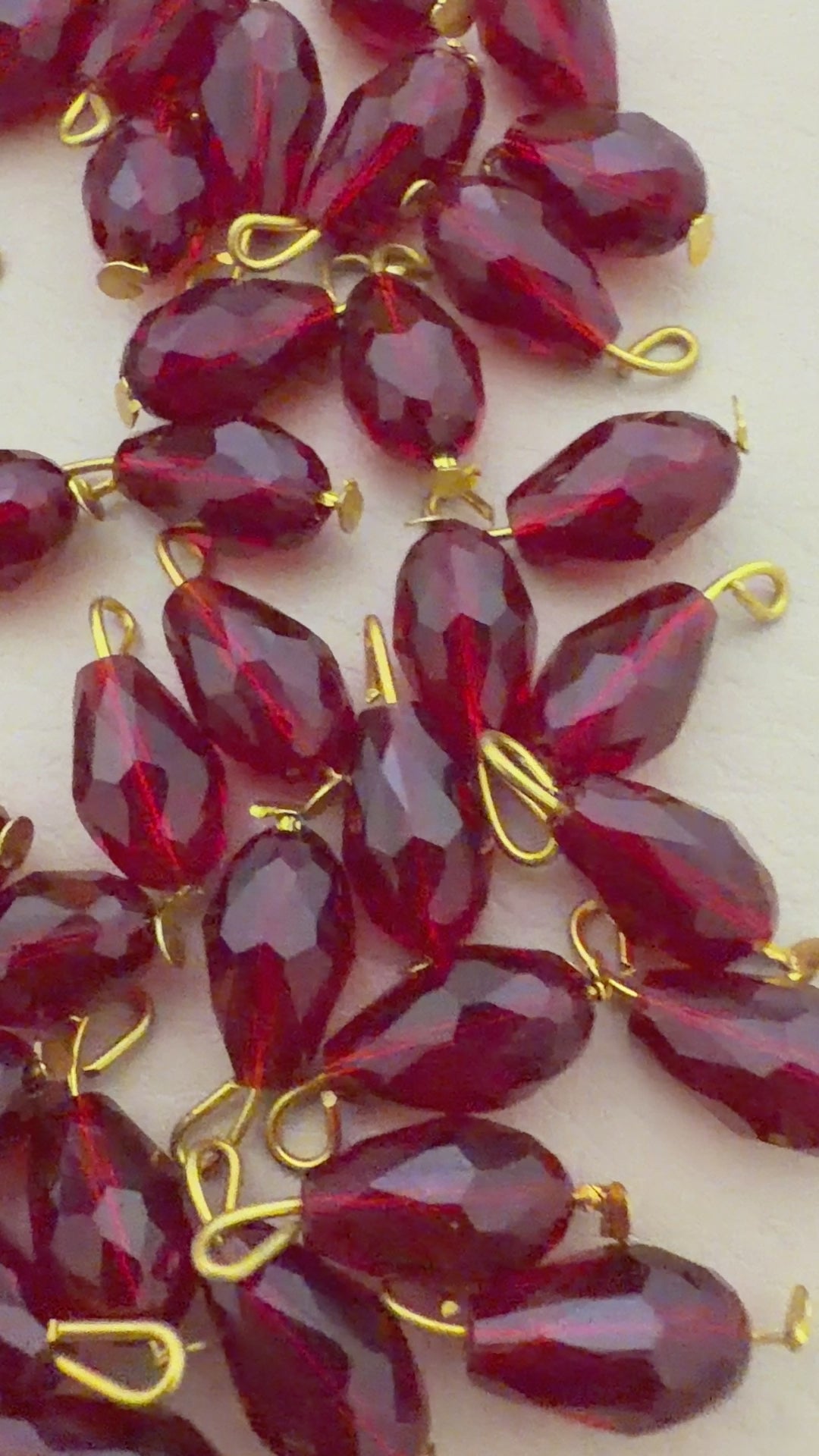 Red teardrop-shaped beads with gold loops on a light beige surface