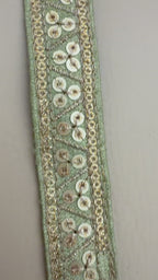 Decorative ribbon with gold embellishments measured against a ruler on a beige background
