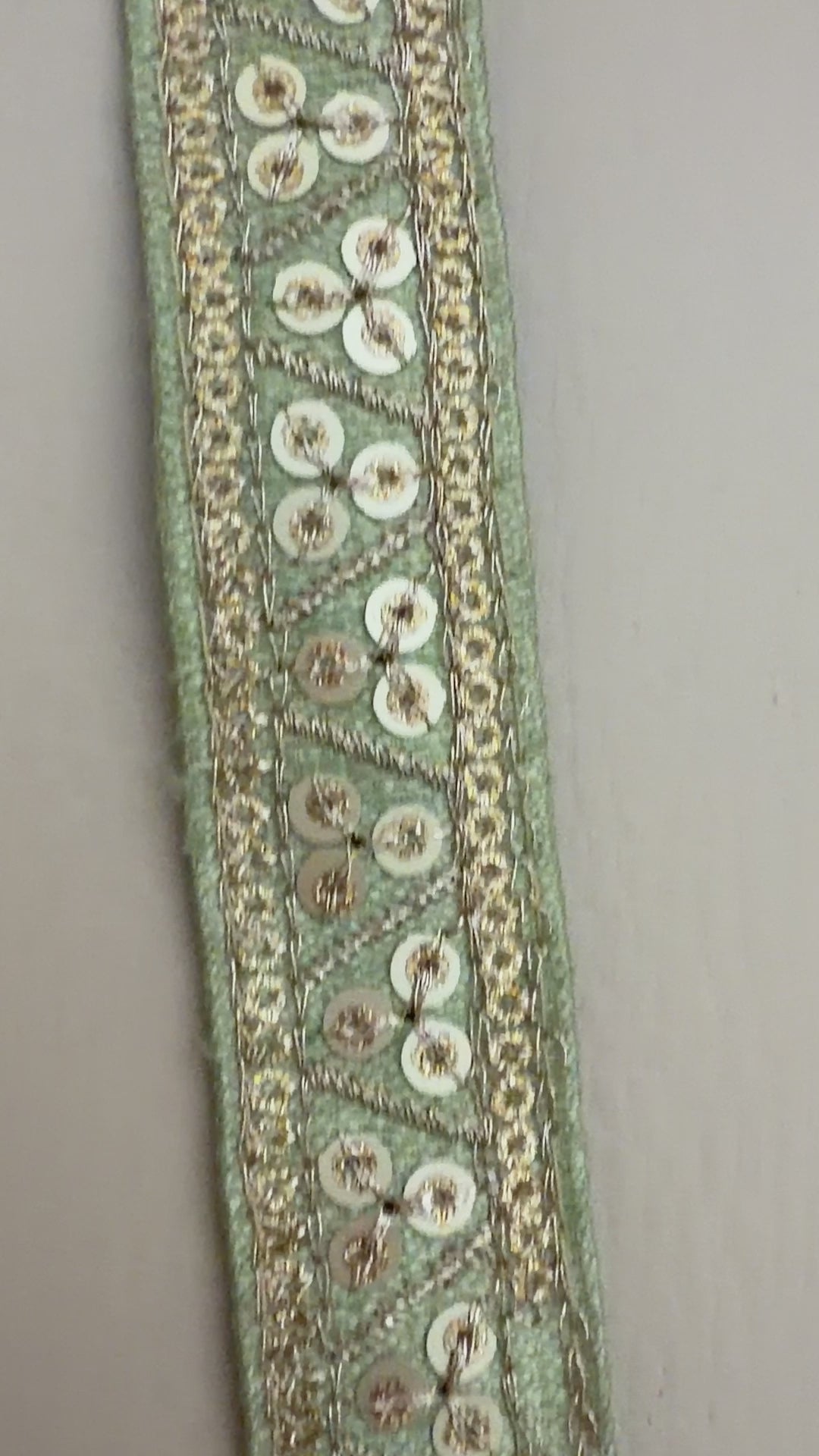 Decorative ribbon with gold embellishments measured against a ruler on a beige background