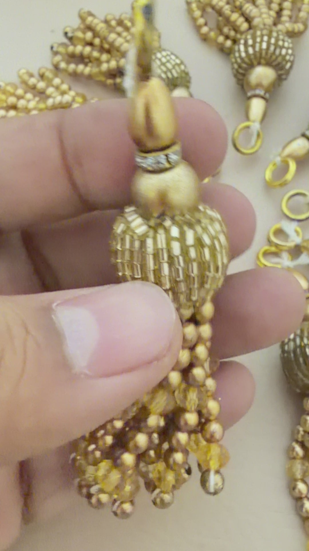 Gold tassel earrings with beads next to a wooden ruler for scale on a light background