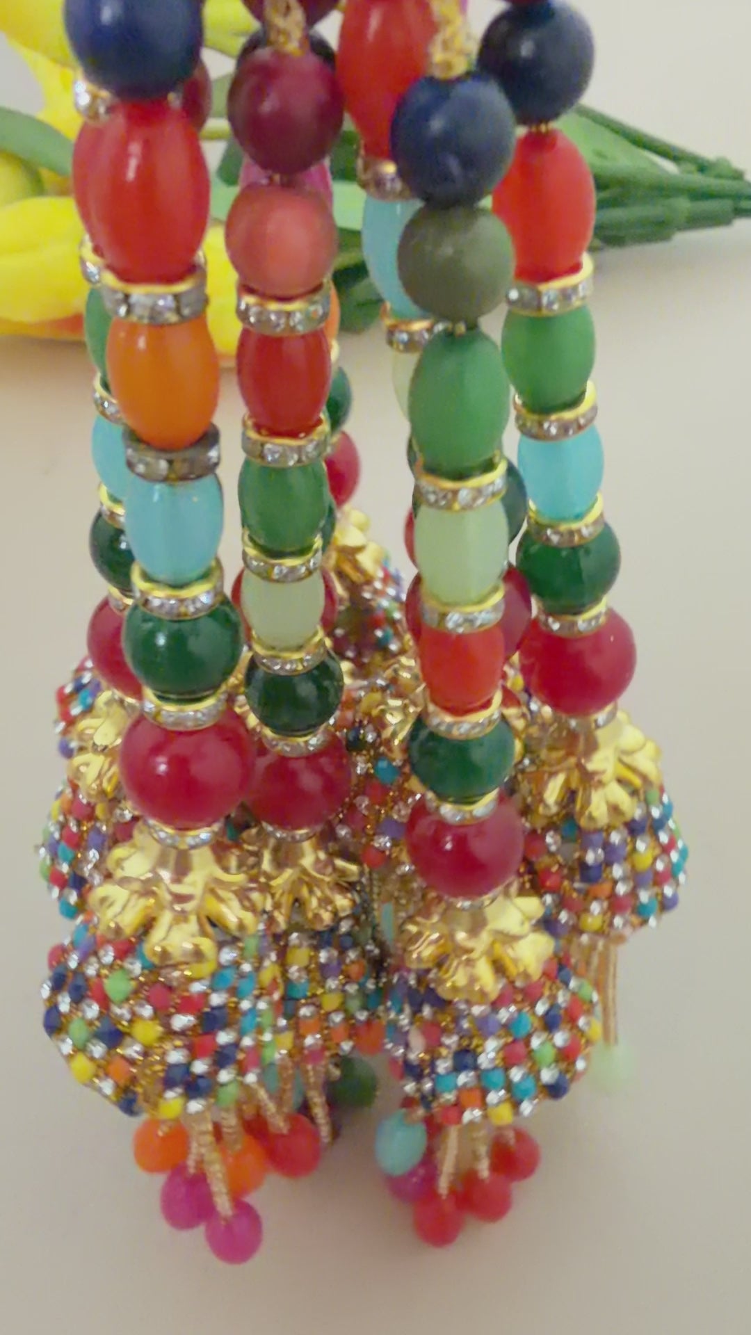 Colorful beaded decorative item held in a hand with flowers in the background