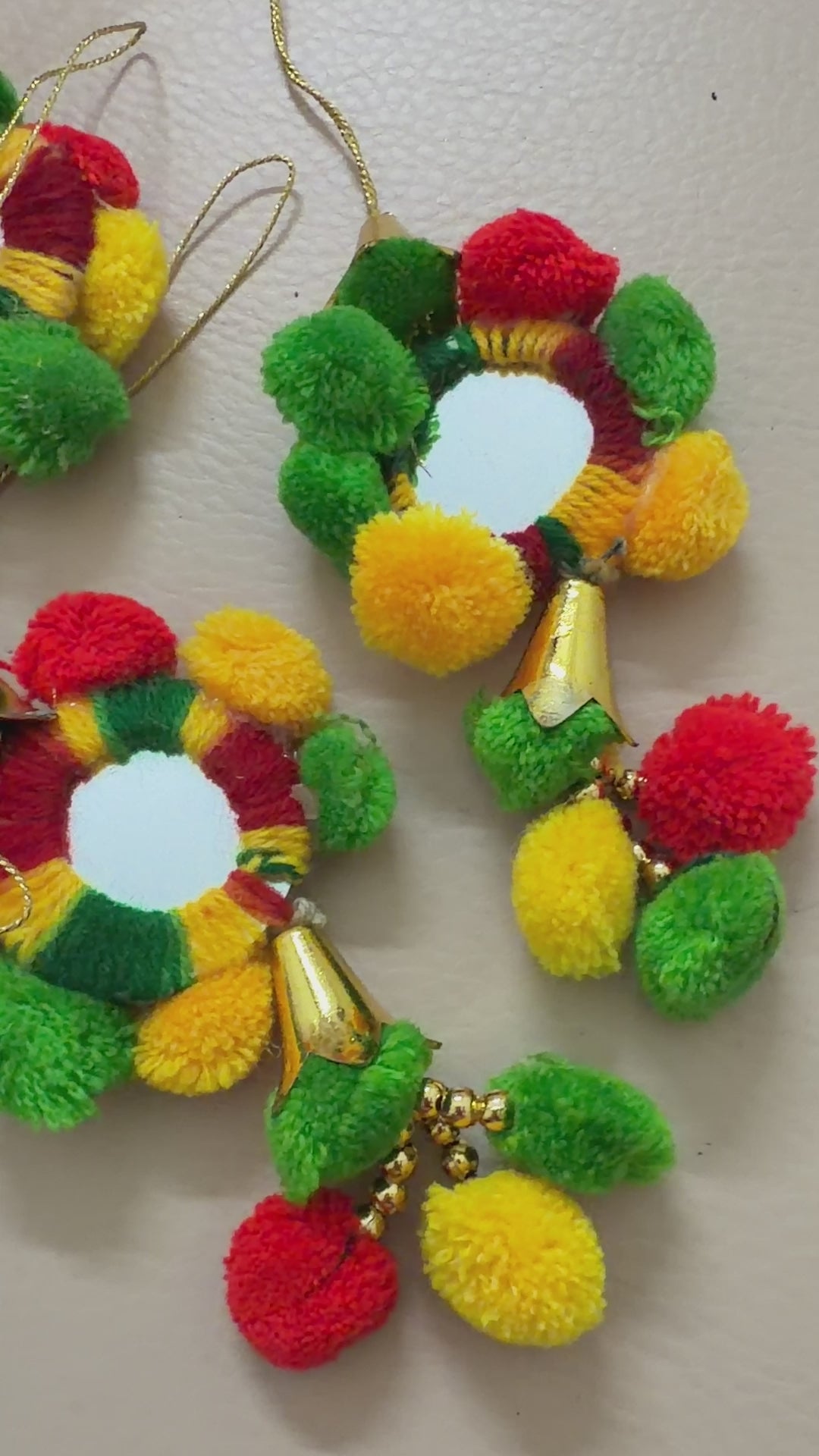 Pair of colorful pom-pom earrings with gold accents on a beige background