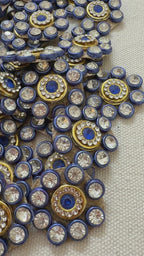 Close-up of decorative embellishments with blue centers and gold and silver accents on a neutral background.