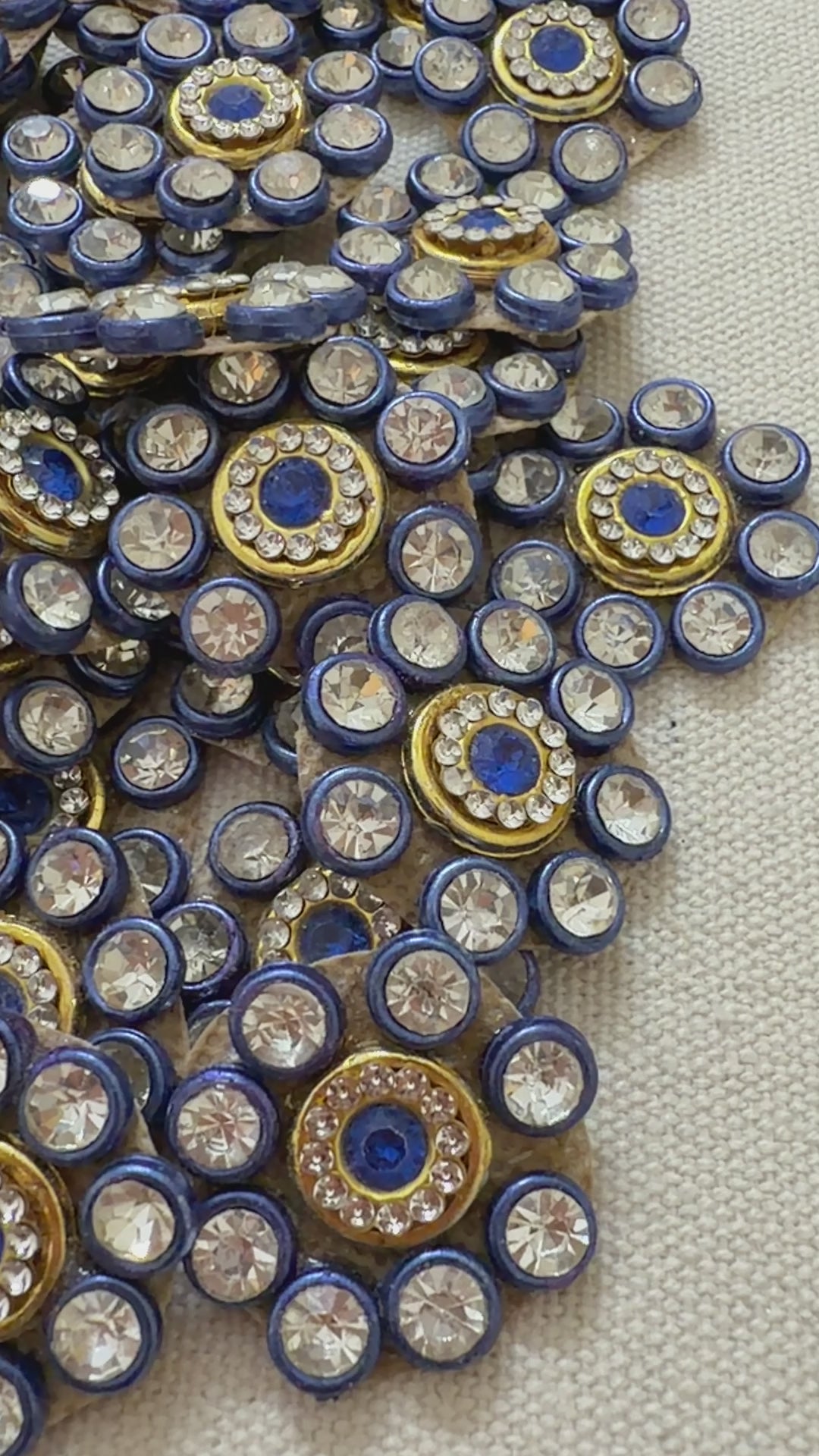 Close-up of decorative embellishments with blue centers and gold and silver accents on a neutral background.