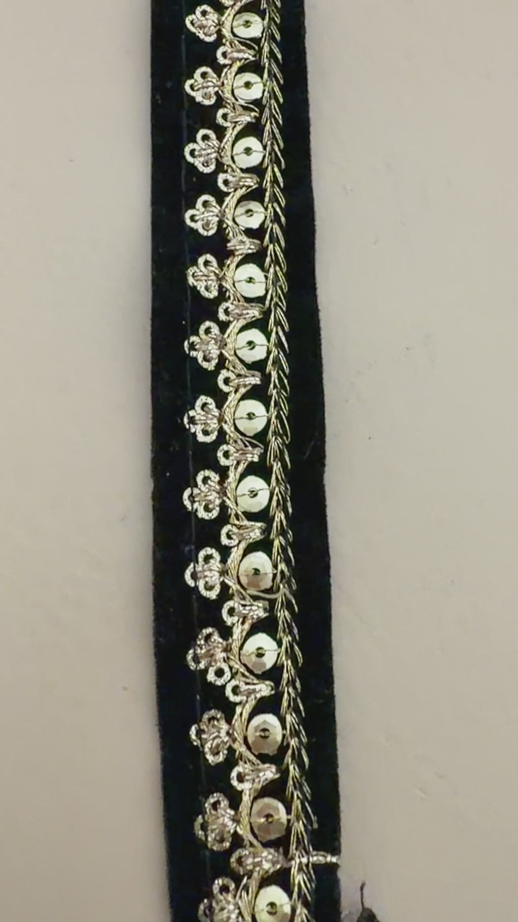 Black clutch with gold embroidery next to a white flower on a beige background