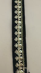 Black clutch with gold embroidery next to a white flower on a beige background